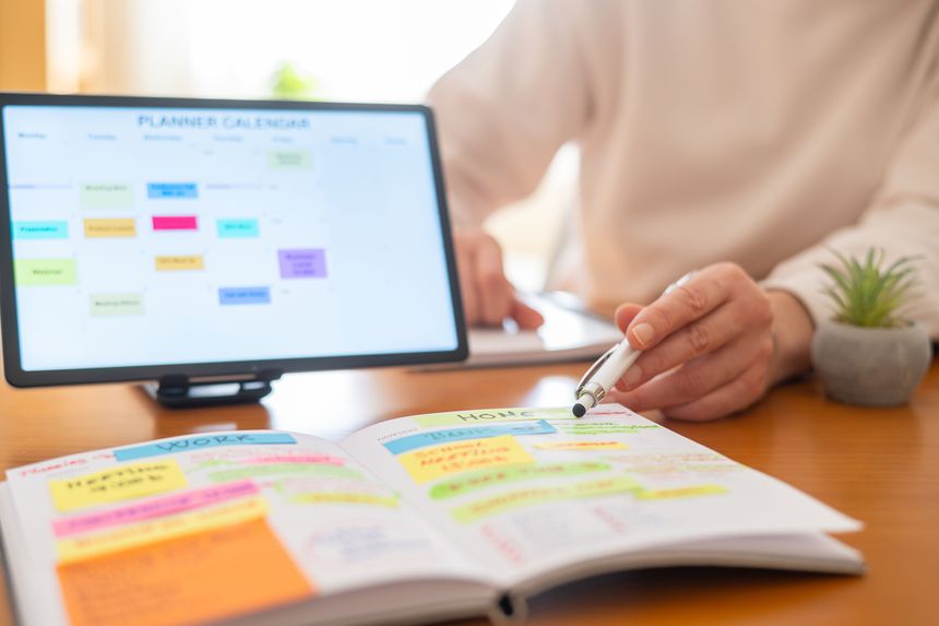 Woman managing daily tasks, appointments, and work life balance by highlighting important events in a physical planner and reviewing a digital calendar on a tablet