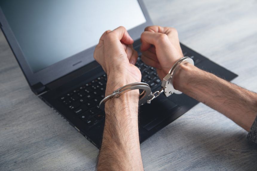 Hacker hands in handcuffs on the laptop.