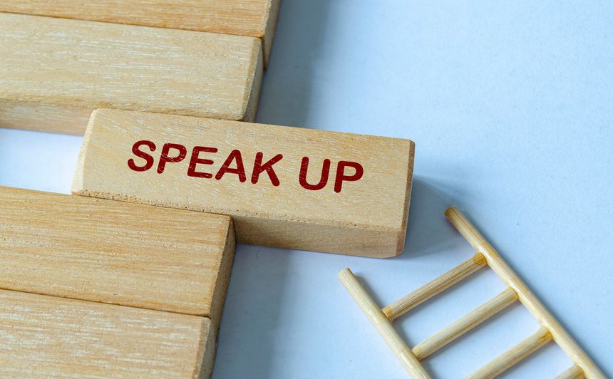 SPEAK UP text on wooden blocks with ladder representing accessible reporting and open dialogue