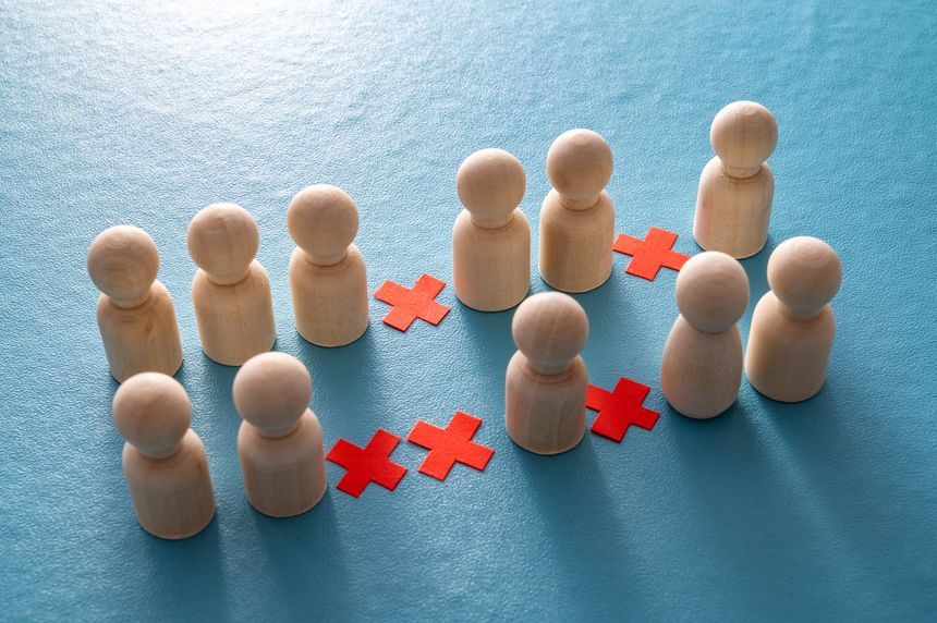 Conceptual representation, with wooden pawns and red crosses, of corporate layoffs. Concept of layoffs, staff cuts, and mass layoffs.