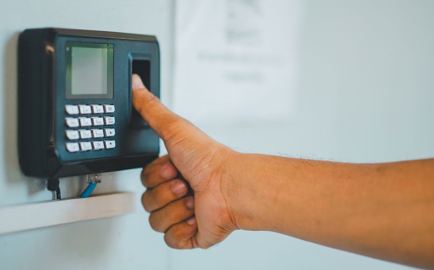 A person is using a fingerprint reader to access a building. The person is giving a thumbs up sign, indicating that the process is going smoothly