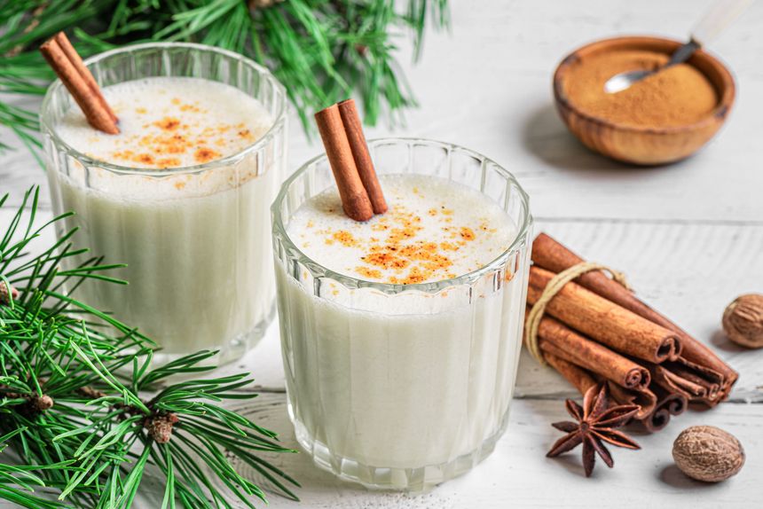 Eggnog cocktail drink (spiced egg-milk) with cinnamon and nutmeg for Christmas and winter holidays. Homemade eggnog in glasses on white wooden background.