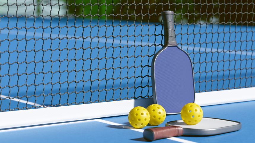 A pickleball paddle and balls resting by the net on a blue court, ready for a game. 3d rendering