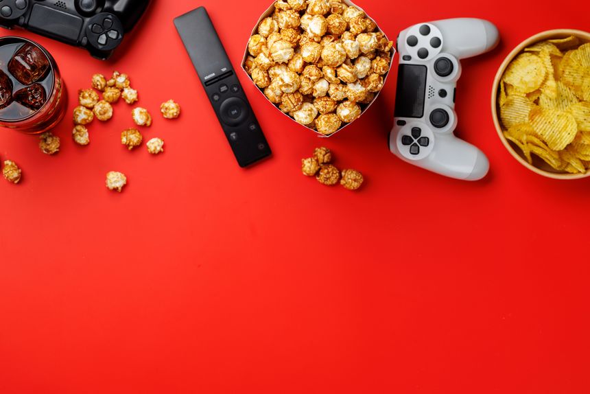 Popcorn in paper bucket with game controller on bright red background, gaming evening entertainment concept