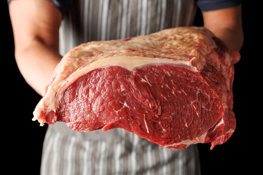 Butcher holding with hands a large piece of beef sirloin steaks.