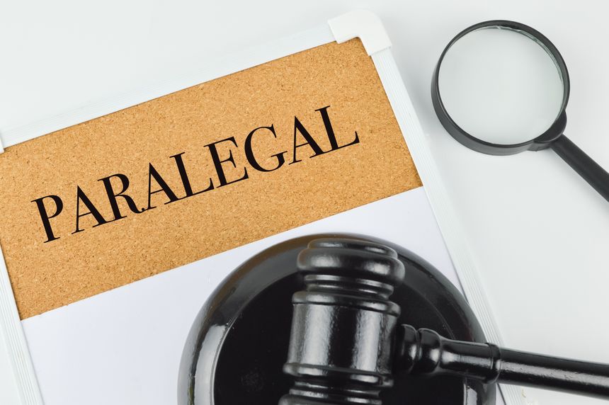 Phrase PARALEGAL written on brown board with judge gavel and magnifying glass.