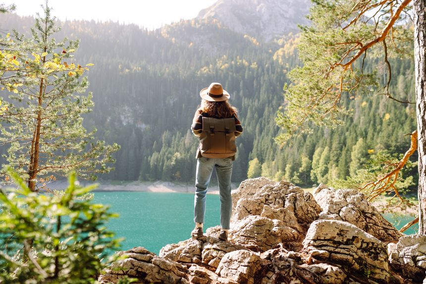 Enjoying a peaceful moment, a woman sits on a rocky ledge while gazing at the stunning turquoise lake surrounded by lush mountains during daylight. Active lifestyle.