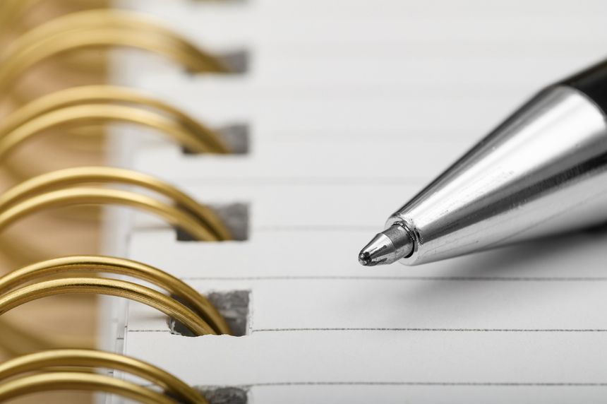 Writing something in a notebook, close-up of a pen lying on a sheet of notebook paper