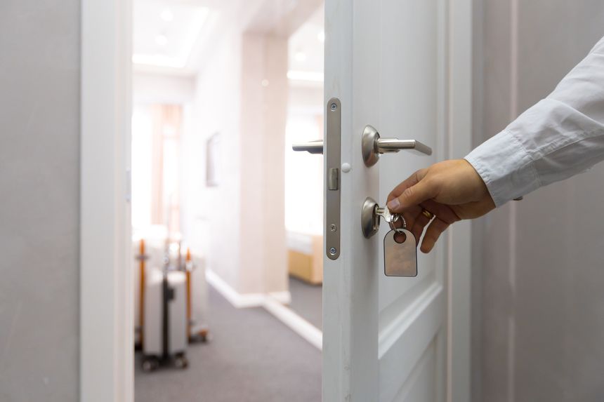 A person is using a key to unlock a door in a bright hotel corridor during the day.