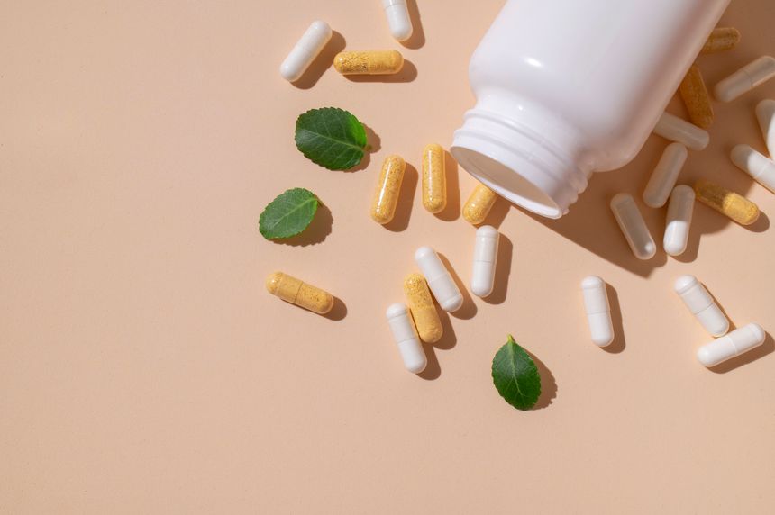 Minimalistic concept of vitamins, dietary supplements, nutraceuticals. Capsules, pills, tablets, white jar, green leaves on beige background. Medical pharmacological background