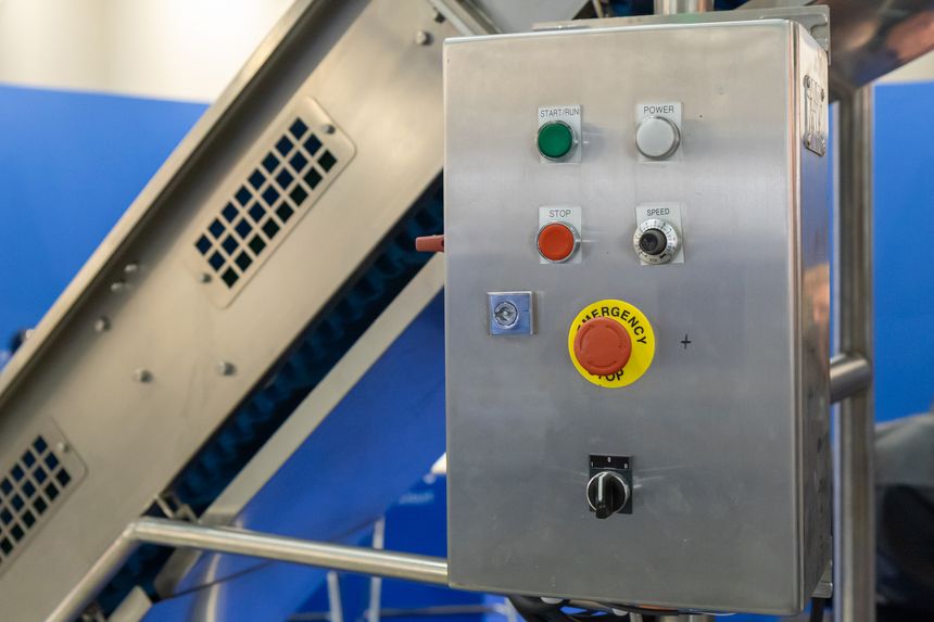 A stainless steel industrial control panel, featuring start, stop, power, and emergency stop buttons, along with a speed dial and key switch, is displayed, indicative of automation technology