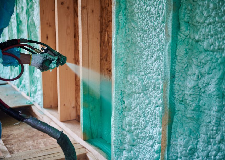 Builder insulating wooden frame house. Close up view of man worker spraying polyurethane foam inside of future cottage, using plural component gun. Construction and insulation concept.
