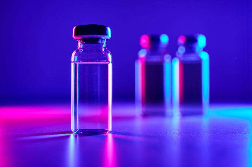 Medical vials with clear solution illuminated by vibrant neon purple and blue lights, representing glp 1 peptide drug research, biotech innovation for diabetes and weight management