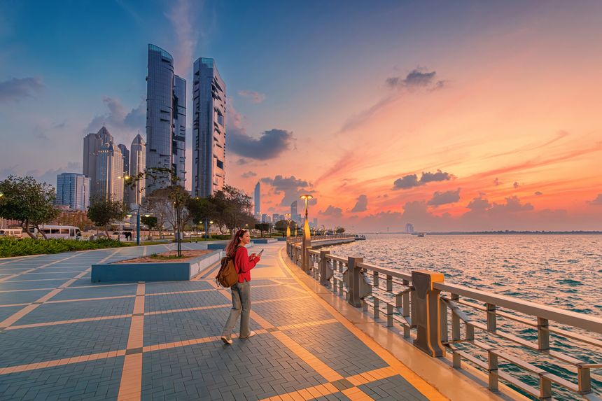 Walking along the Abu Dhabi Corniche promenade at sunset, enjoying the vibrant cityscape and serene waterfront views of modern skyscrapers