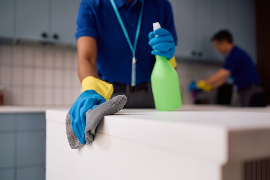 Close up of female professional cleaner cleaning countertops in corporate kitchen.