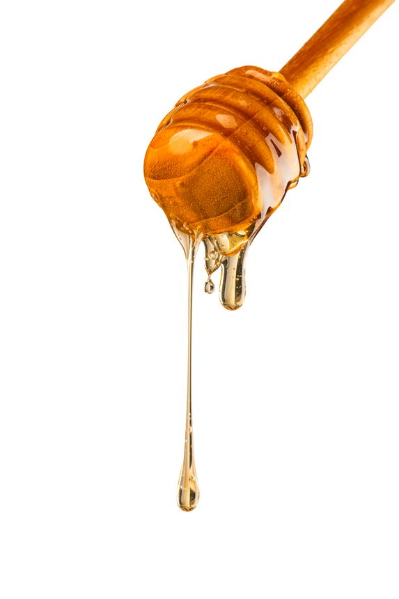 Golden Honey Dripping from Wooden Honey Dipper onto Jar full of Fresh Honey With Honey Comb in the Background