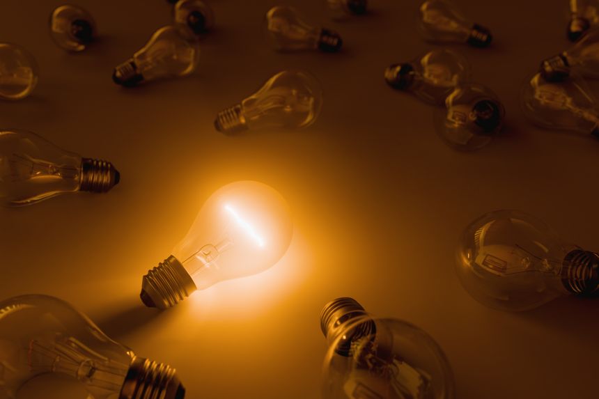 A glowing light bulb stands out among several unlit bulbs on a dark background.