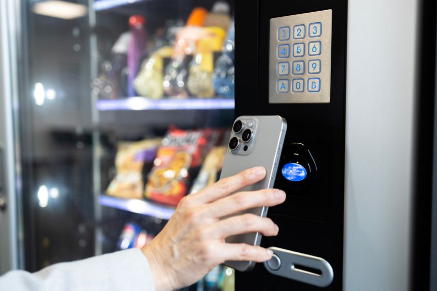 Close up view of woman hand holding smart phone and making contactless payment, buying snacks on vending machine.