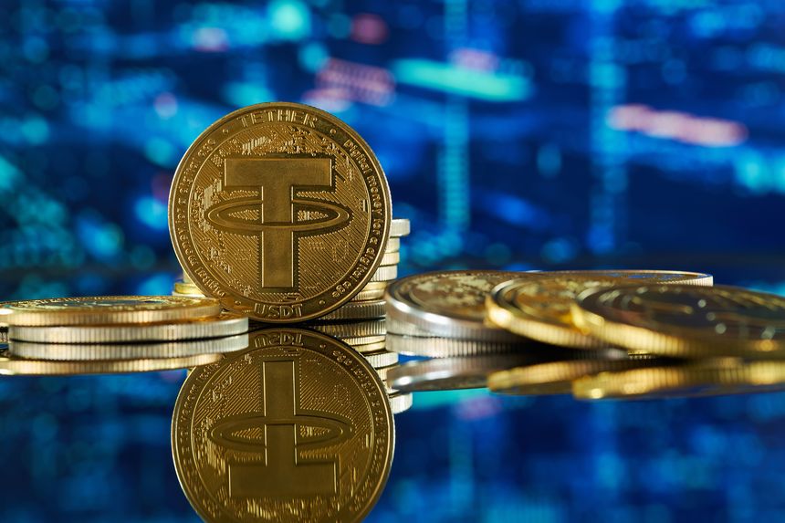 Golden Tether cryptocurrency placed on a reflective surface, surrounded by additional coins, with a blurred digital screen in the background.