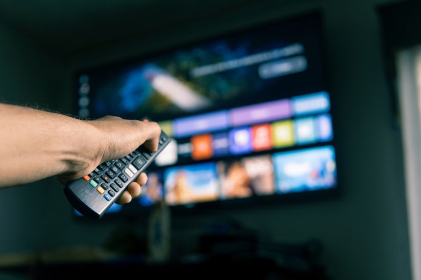 Hand holding a remote control, browsing streaming services on a smart tv