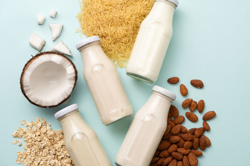 Types of plant-based milk in glass bottles. Coconut, rice, almond and oat milk on blue background