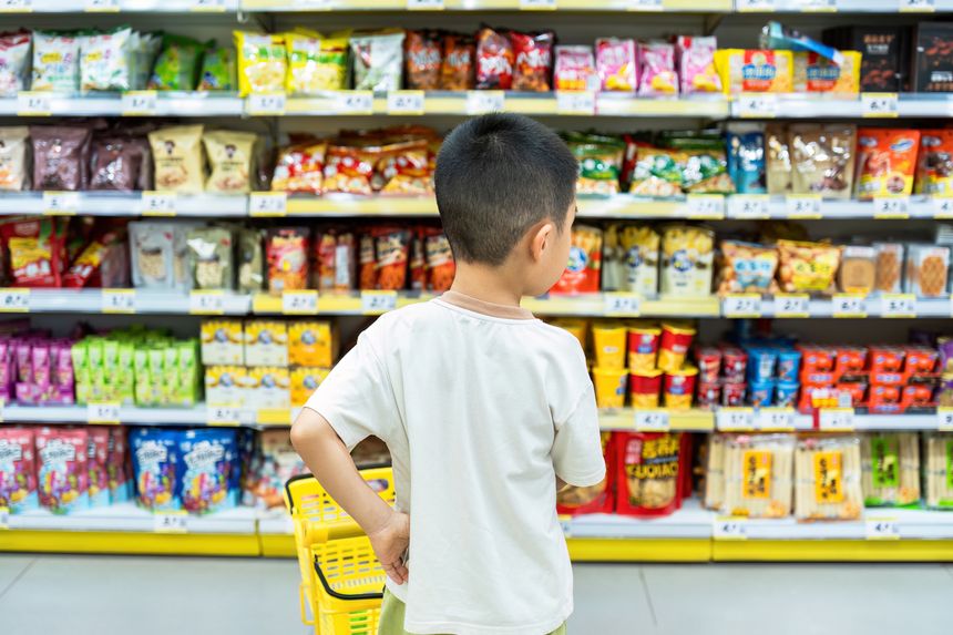 A cute Asian boy was pushing a shopping cart and shopping at the snack store.