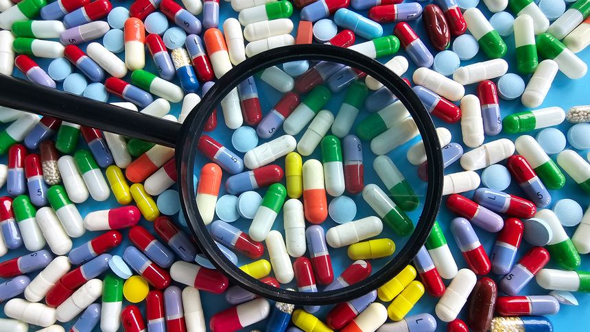 Many colorful pills and capsules spread across a surface with a magnifying glass on them