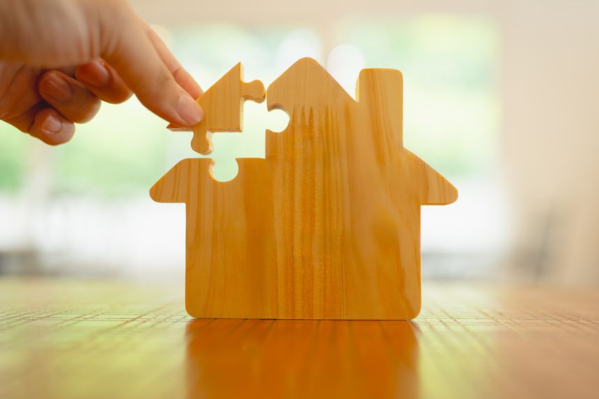 Hand Holding the Key to Real Estate: Unlocking Property Dreams with a House Puzzle.
