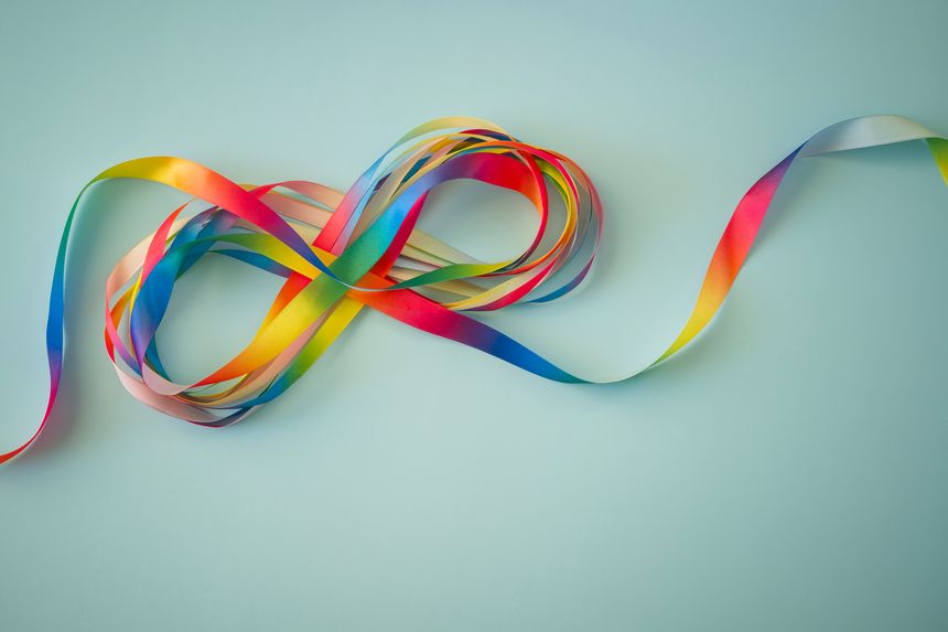 Autism acceptance month, Autism awareness day concept. Rainbow colors ribbons in shape of infinity loop on blue background. Infinity is symbol of autism disorder, adhd, neurodiversity. Top view