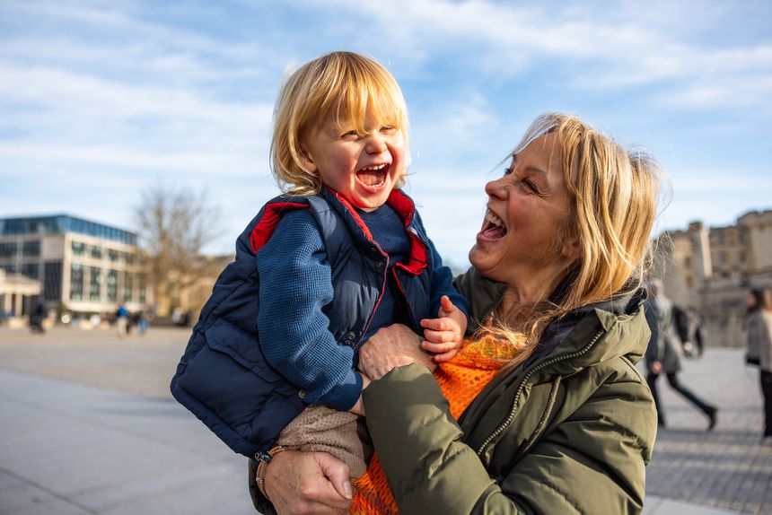 Grandmother holding her grandson, both laughing and enjoying a sunny day in the square near the Tower of London, showing family love and connection