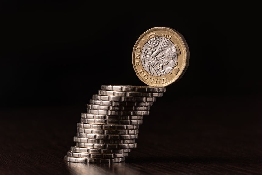 One British pound coin and a column of coins on a black background