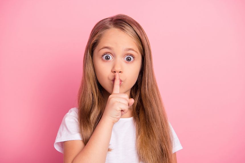Portrait of little nice girl finger cover touch lips demonstrate shh gesture isolated on pink color background.