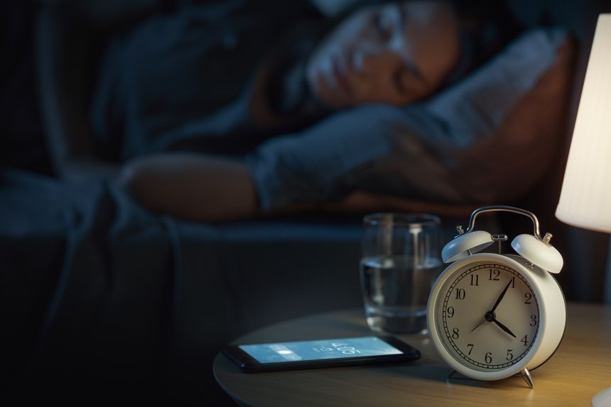 Young woman sleeping in bed and alarm ringing on her smartphone early in the morning