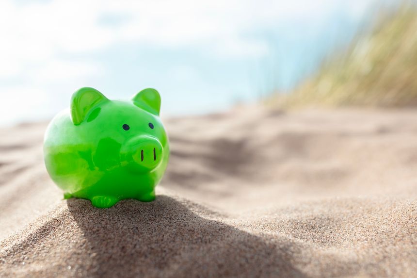 Green piggy bank on beach holiday sitting on the sand at the seaside