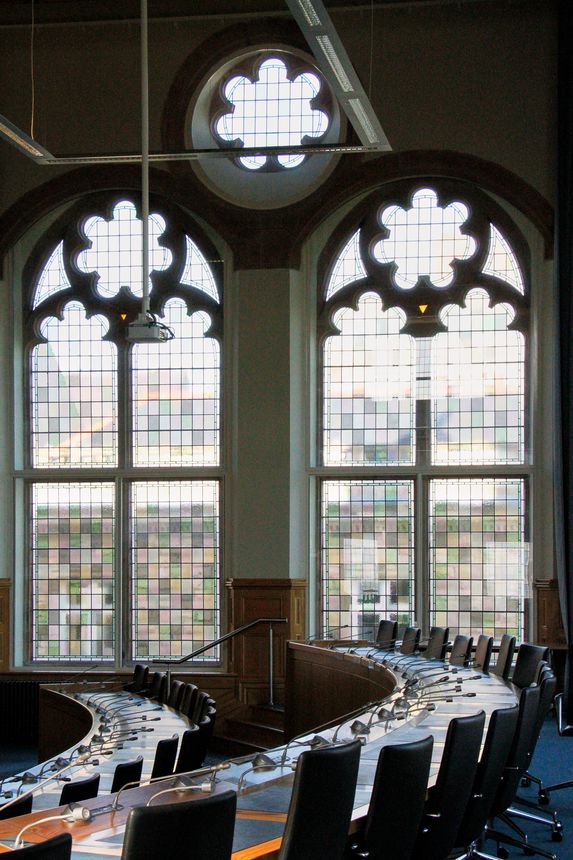 Tall arched stained glass windows line the council chamber of the Guildhall in Derry, Northern Ireland. The colorful panes cast soft light into the room where civic decisions are made.