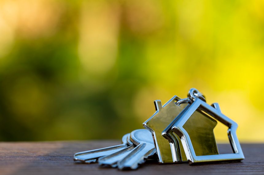 House keys on a house shaped keychain on wooden table, outdoors, close up, copy space. Real estate concept of buying or renting a home
