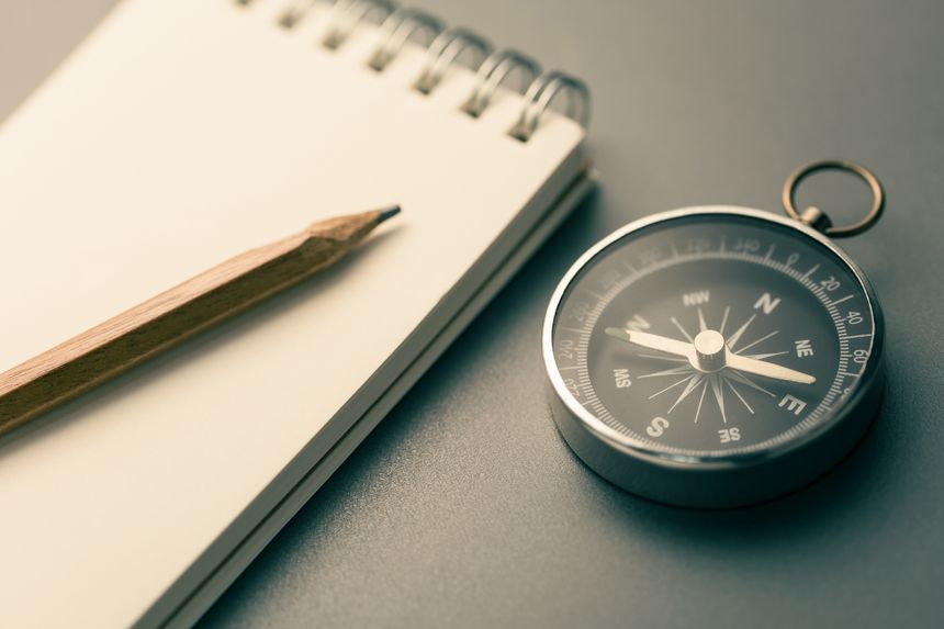 Close-up of a compass beside a pencil and notebook, symbolizing clarity, direction, and purpose in writing, planning, and effective communication