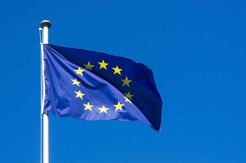 Low angle view of the official European Union flag with twelve yellow stars waving in the wind. Minimalist composition under a clear bright blue summer sky background with copy space. Concept of European geopolitics, economy, unity and international relations