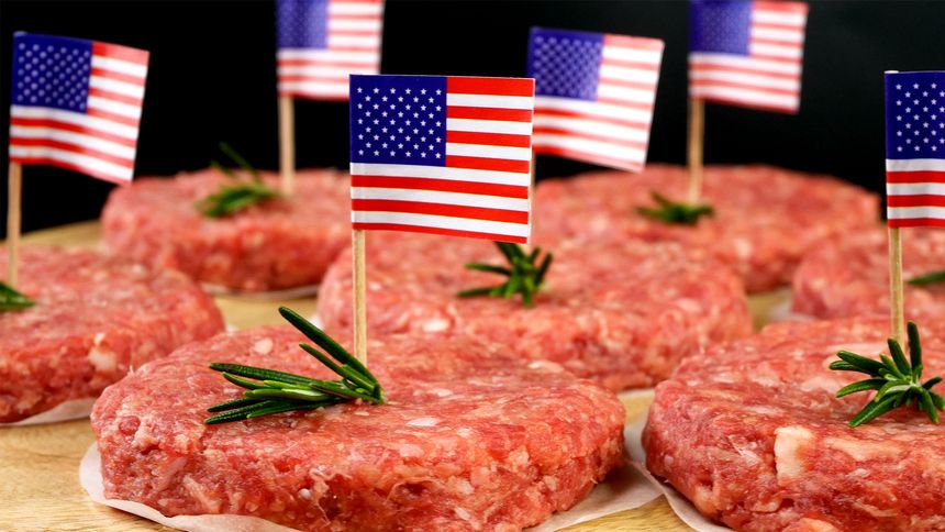 Round fresh raw mince beef burger cutlets with american flag and rosemary sprigs. Preparation food for Independence Day on domestic kitchen. Close up.