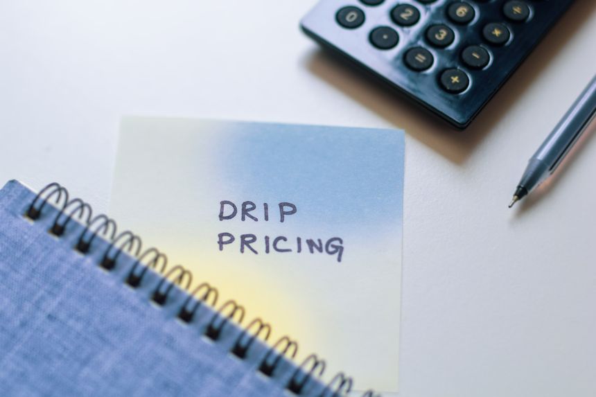 Drip pricing note on desk with calculator, meaning additional fees taxes in purchase process on the advertised price in online retail techniques.