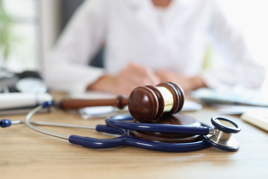 Closeup of judge gavel of stethoscope doctor in background writing notes. Concept of legal aspects of healthcare and medical insurance payments