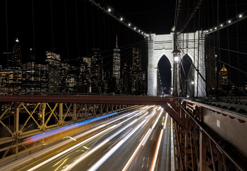 cars driving over the brooklyn bridge at night (light trails long exposure headlights tail lights) manhattan new york city skyline background (dark sky) traffic congestion over east river crossing