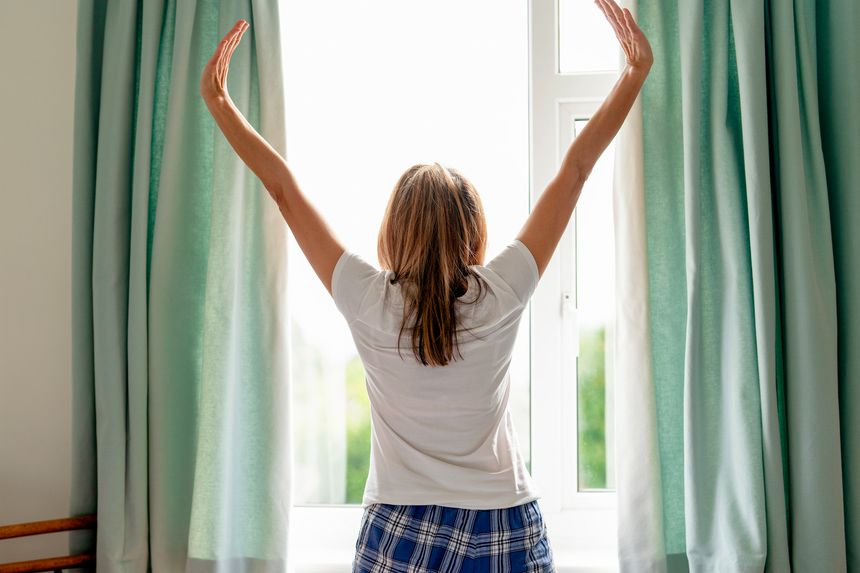 A woman enjoys a refreshing morning stretch by a window, letting in natural light and creating a cheerful atmosphere in her cozy room.