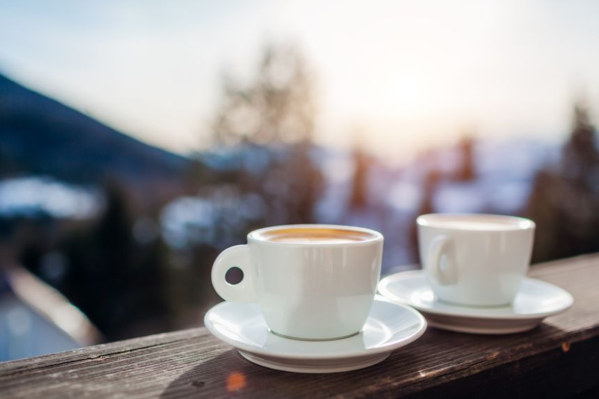 Close up of coffee for two in winter mountains during holidays. Couple of white cups with hot drinks on hotel balcony. Having morning beverages with peaceful snowy landscape