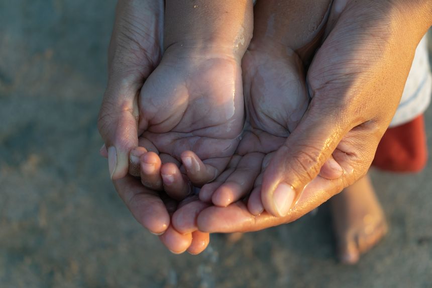 Close-up of an adult holding a child’s cupped hands together with water, symbolizing care, love, protection, and bonding. Concept of family, trust, and nurturing in nature outdoors, water conservation
