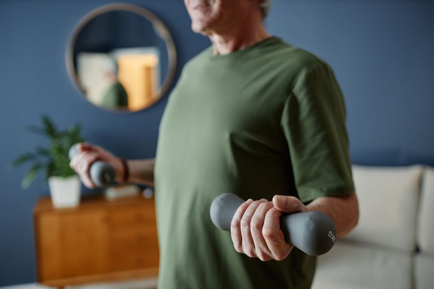 Senior person in green shirt lifting dumbbells indoors with reflection in background mirror and blurred interior, exercising for fitness and strength building