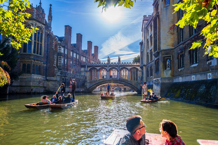 Cambridge, England, UK - October 27, 2024: A vibrant scene on Cambridges River Cam, with people punting near historic university buildings, framed by the iconic Bridge of Sighs and autumn foliage.