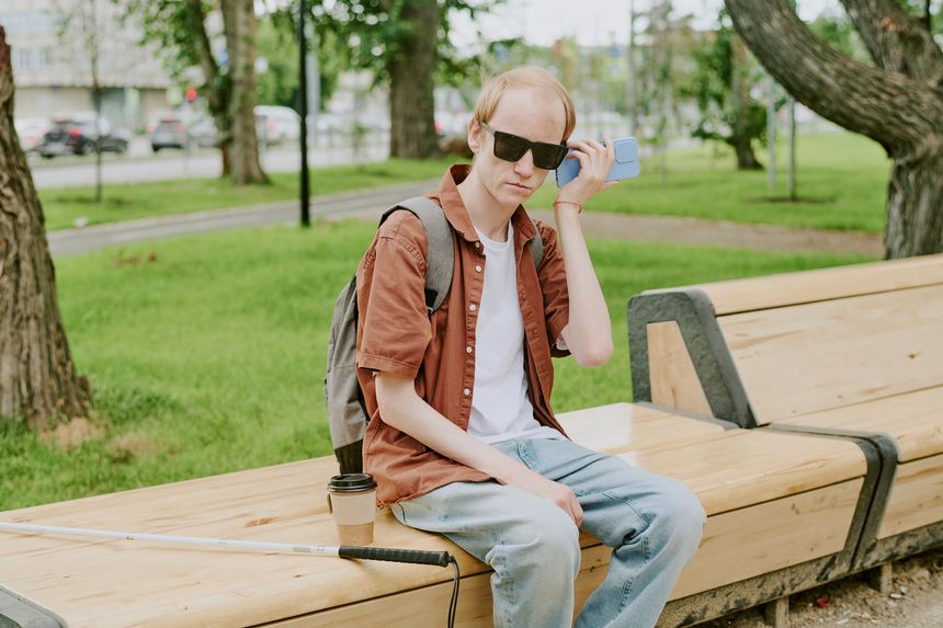 Caucasian man with disability listening to voice message while resting on wooden bench after walk