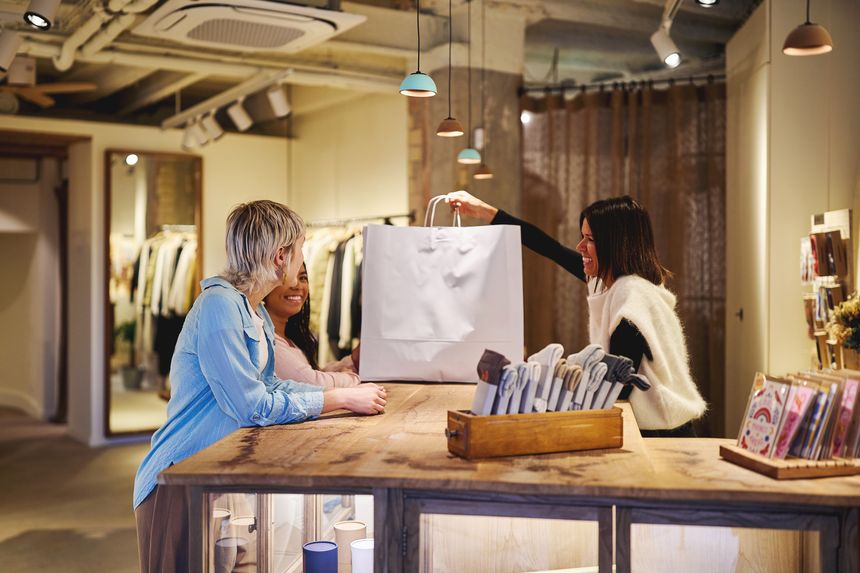 Shop assistant handing shopping bag to smiling customers in boutique