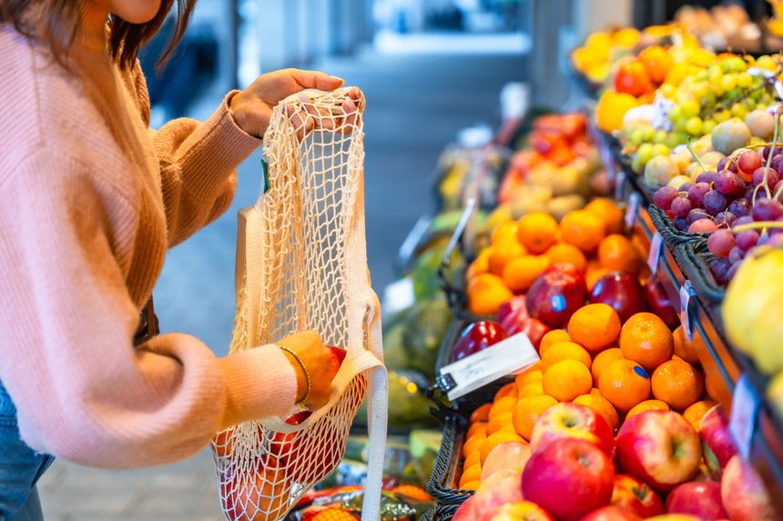 Woman selects ripe red apples at a local market, placing them in a reusable string bag to promote healthy eating, zero-waste shopping and sustainable living